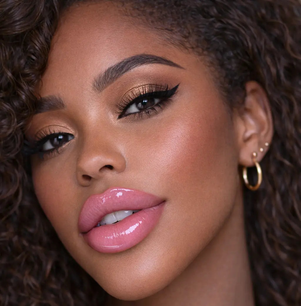 Close-up of a woman wearing diamond glow pink milkshake lip gloss with curly hair
