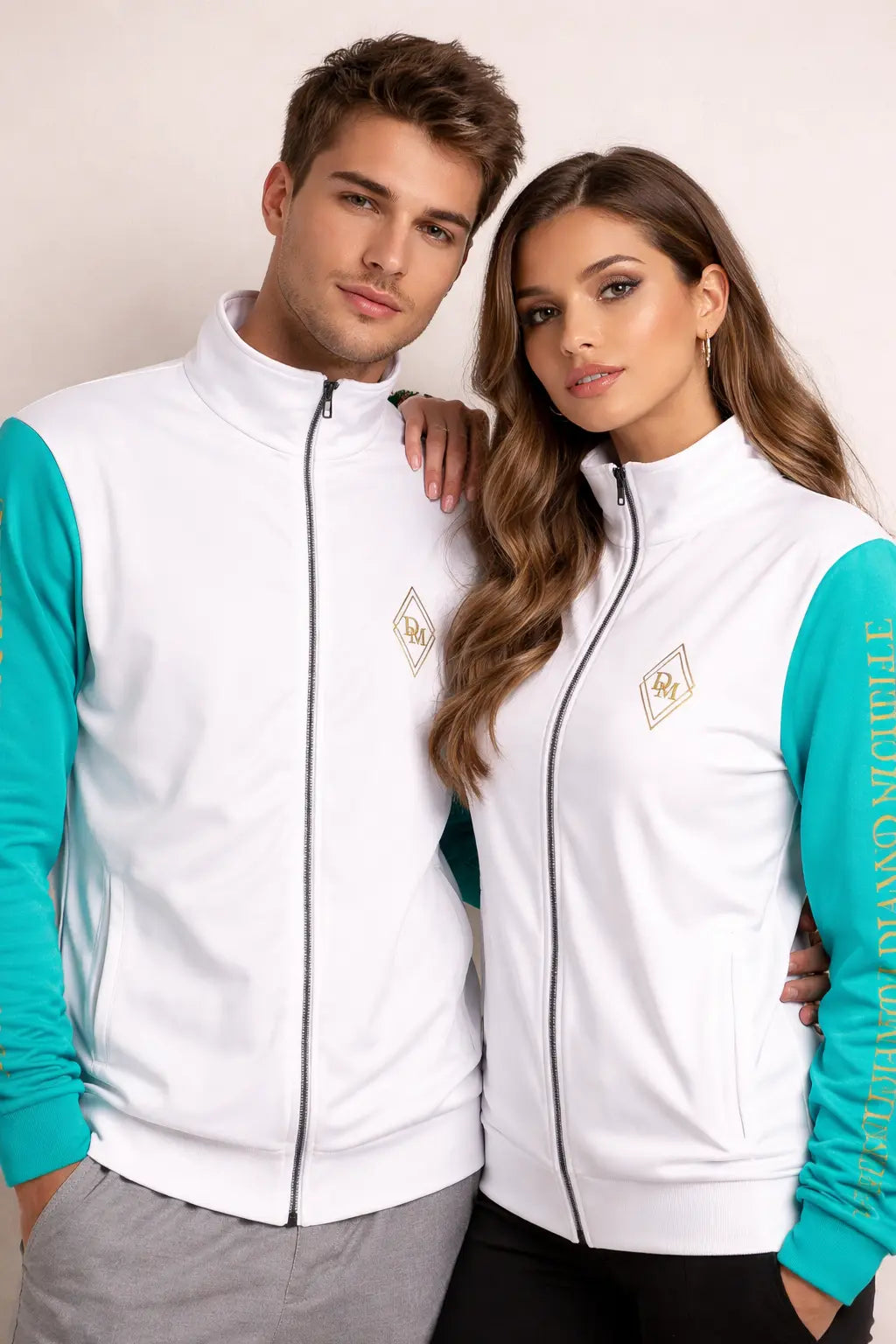 Two people wearing matching white jackets with teal sleeves against a plain background