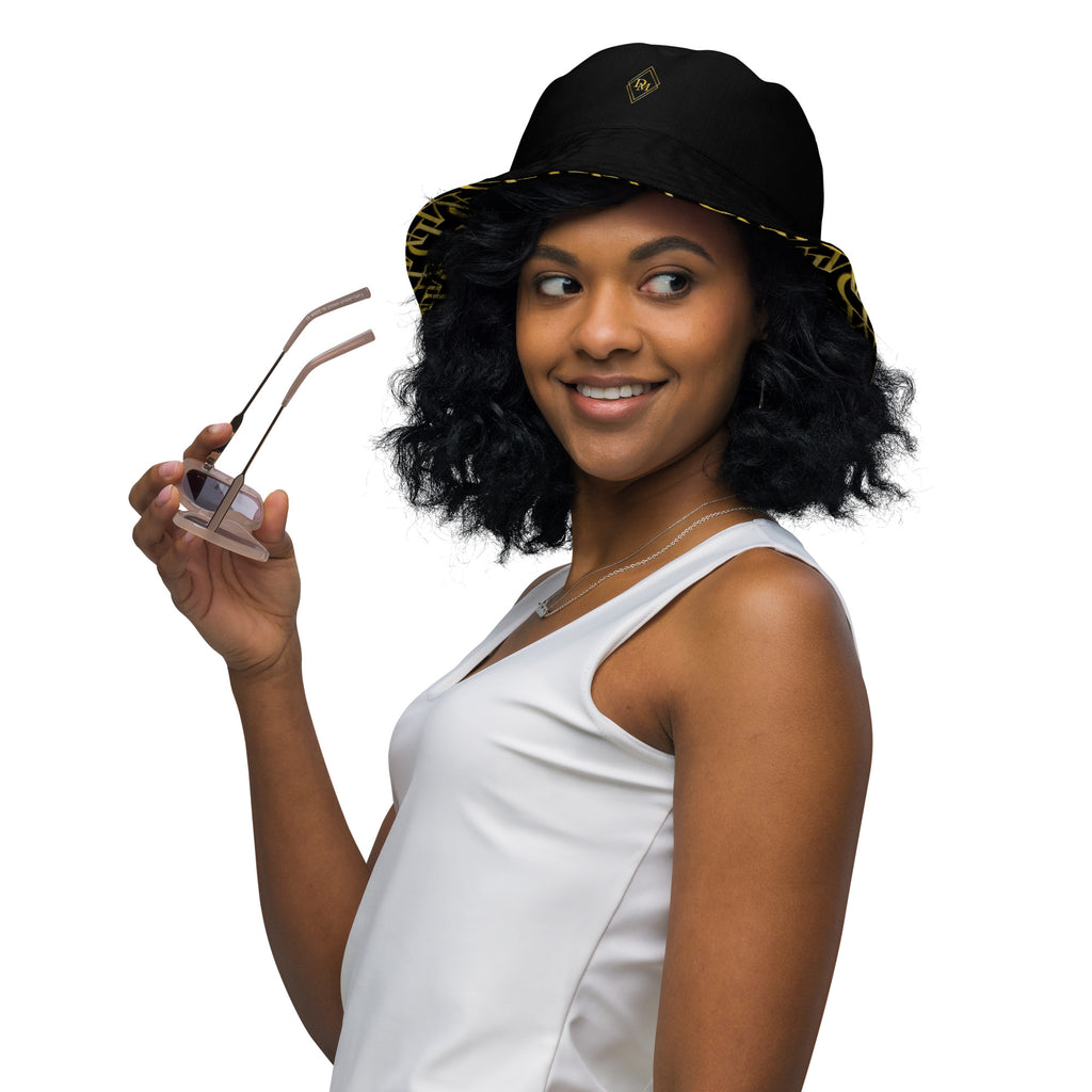 Woman wearing a black bucket hat with gold accents, holding sunglasses, on a white background