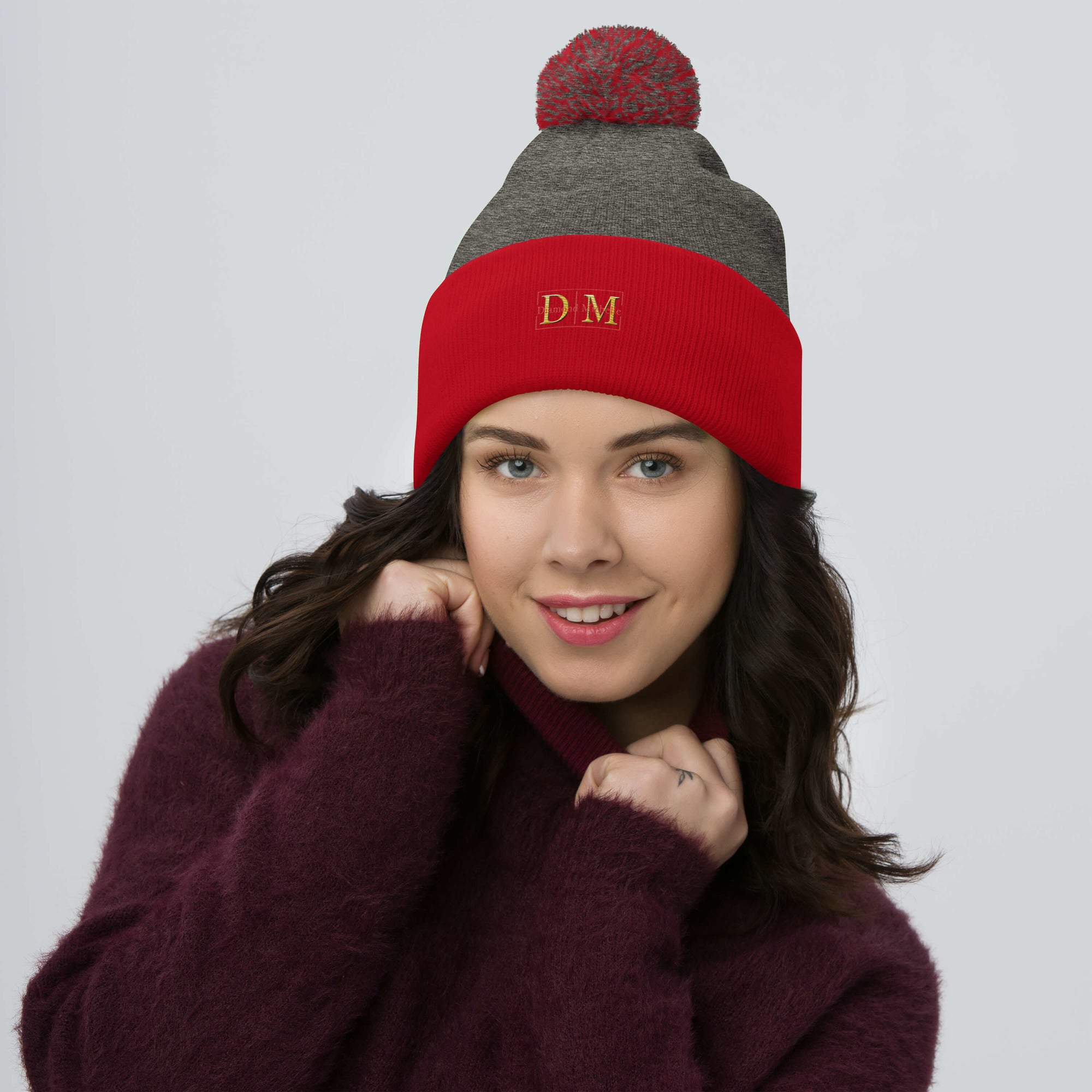 Woman wearing a dark heather grey and red DM Pom-Pom Beanie front view