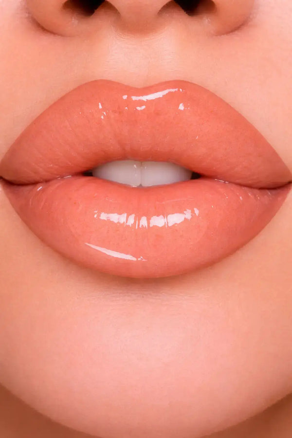 Close-up of glossy peach lip gloss on lips with a neutral background